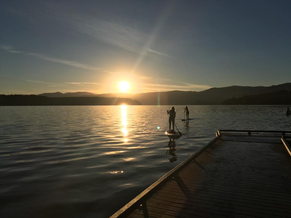 Paddleboarders near a wooden dock at sunset
